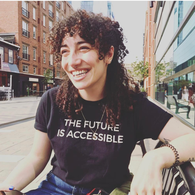 Image of a woman with curly brown hair and a black tshirt that says the Future is Accessible